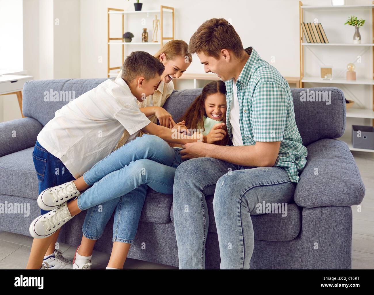 Happy funny family playing on sofa at home, tickling each other, laughing and having fun Stock Photo