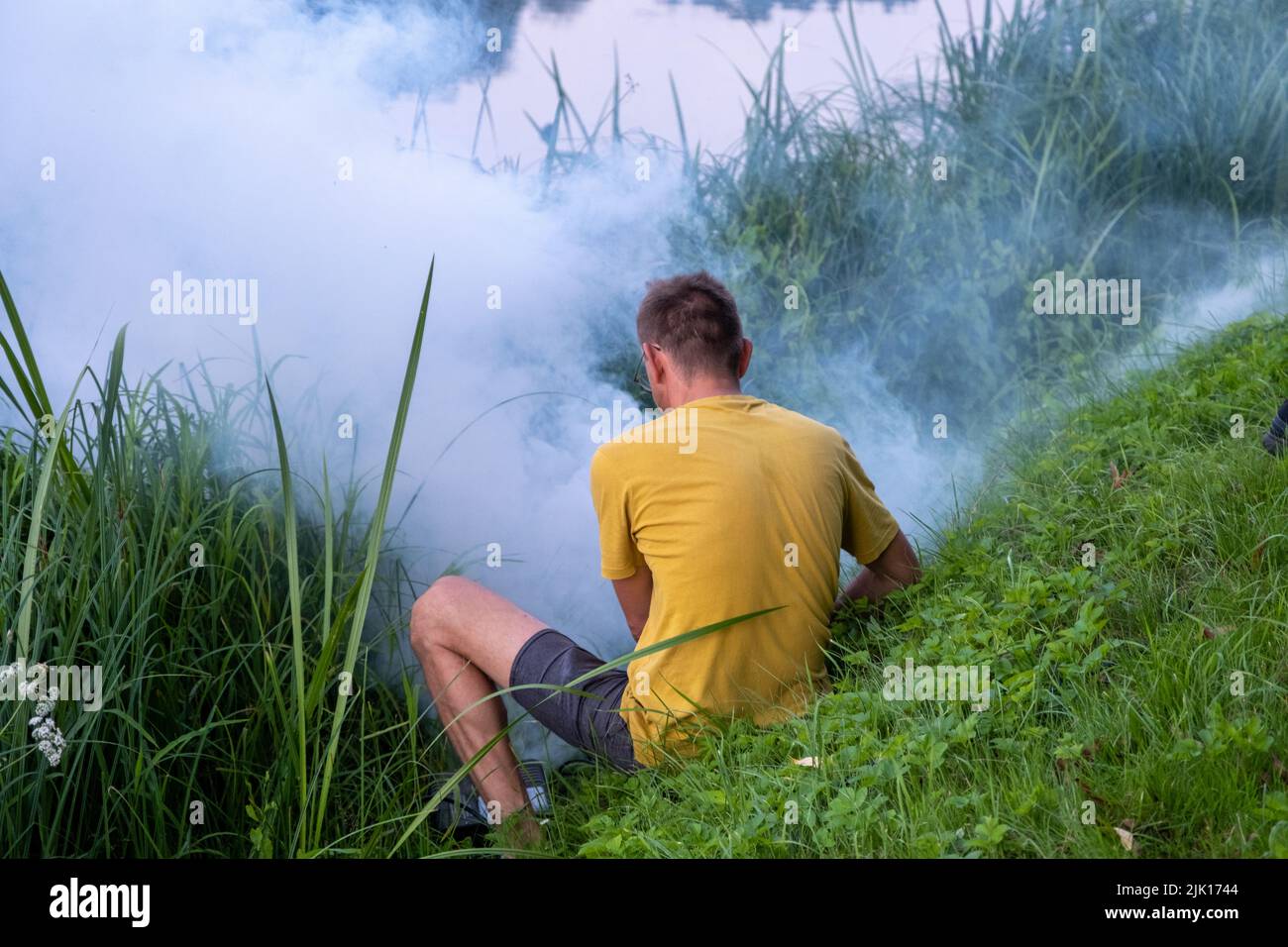 A man in a yellow shirt sets up a smoke machine for an event in nature. Stock Photo
