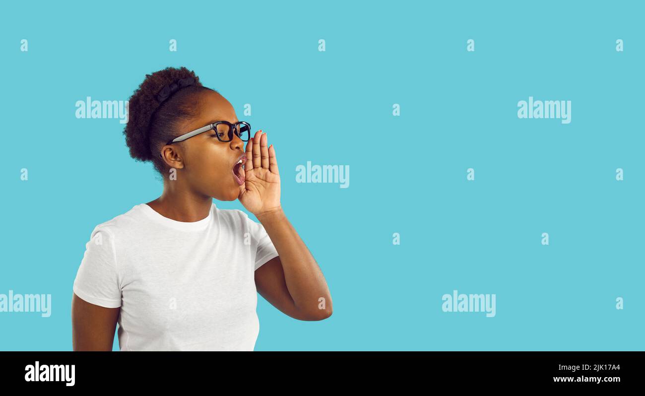African American woman talking or shouting with hand at mouth on blue copy space background Stock Photo