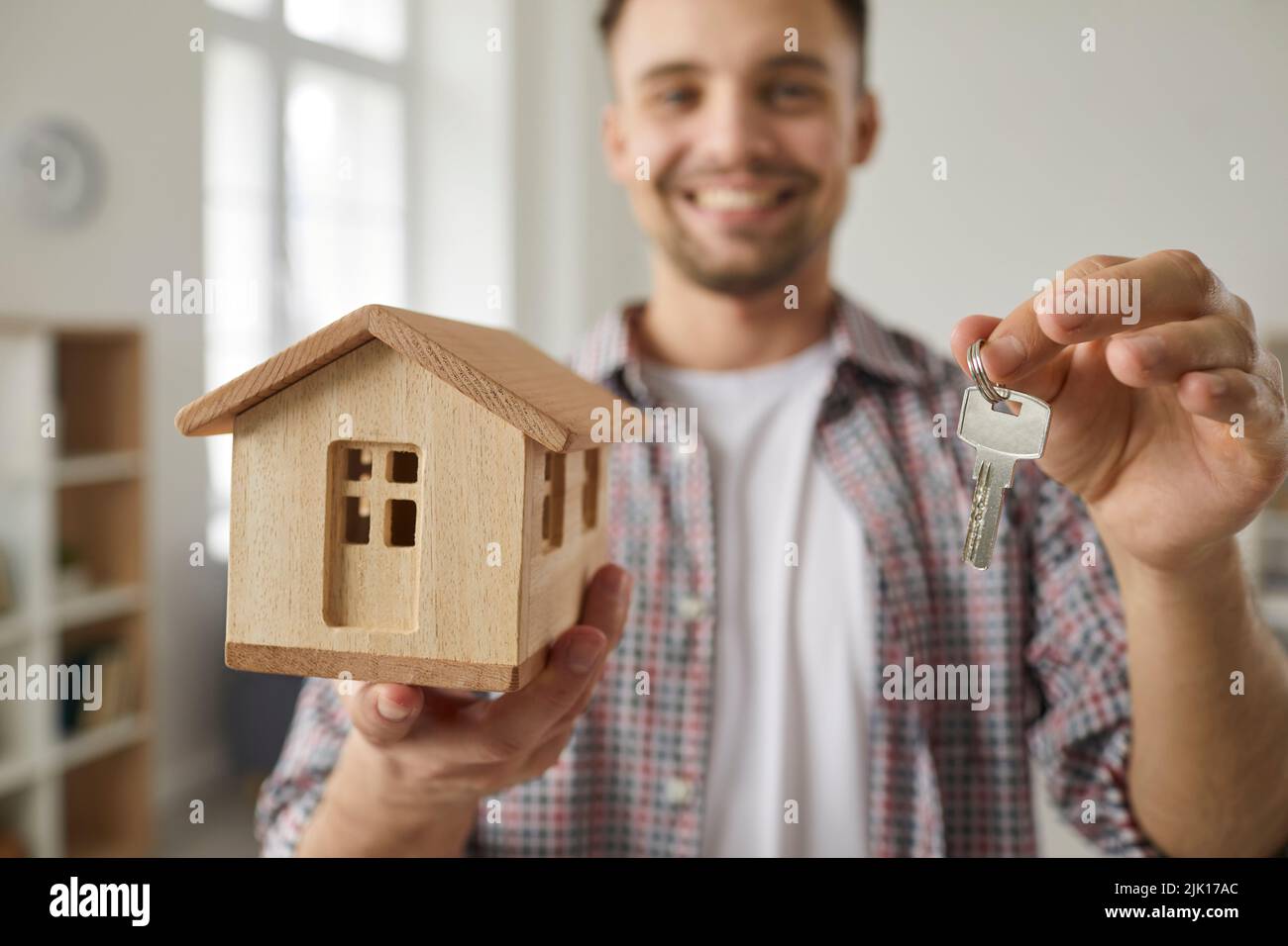 Close up of key and small wooden house model in hands of happy male real estate buyer. Stock Photo