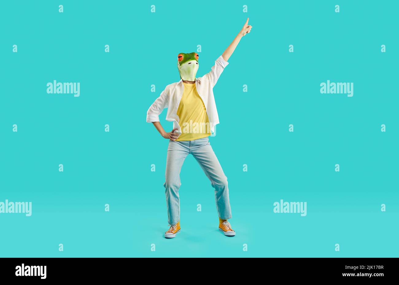Cheerful woman with frog head shows funny dance moves having fun on light blue background. Stock Photo