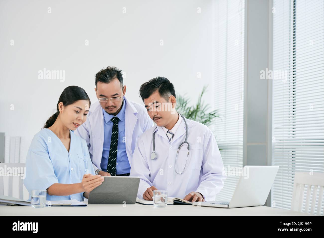 Asian team of medical workers discussing information on tablet computer Stock Photo