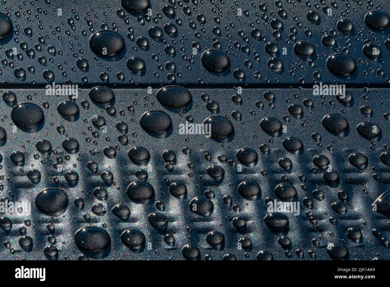 Large to smaller beads of clear water droplets on a medium gray