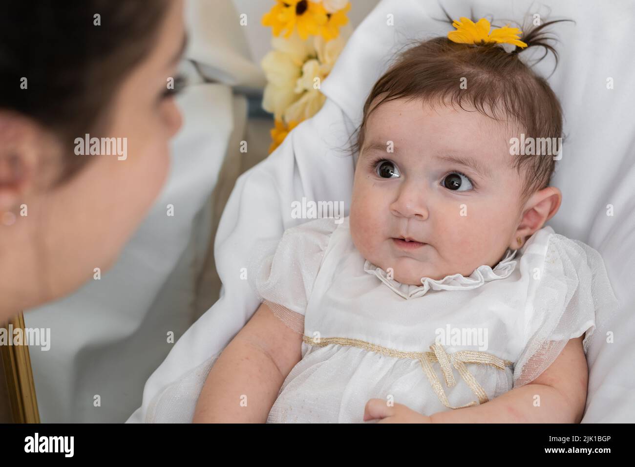 beautiful dark eyed latina baby lying on her crib looking at her mother. young mother spoiling her six month old baby girl. concept of motherhood and Stock Photo