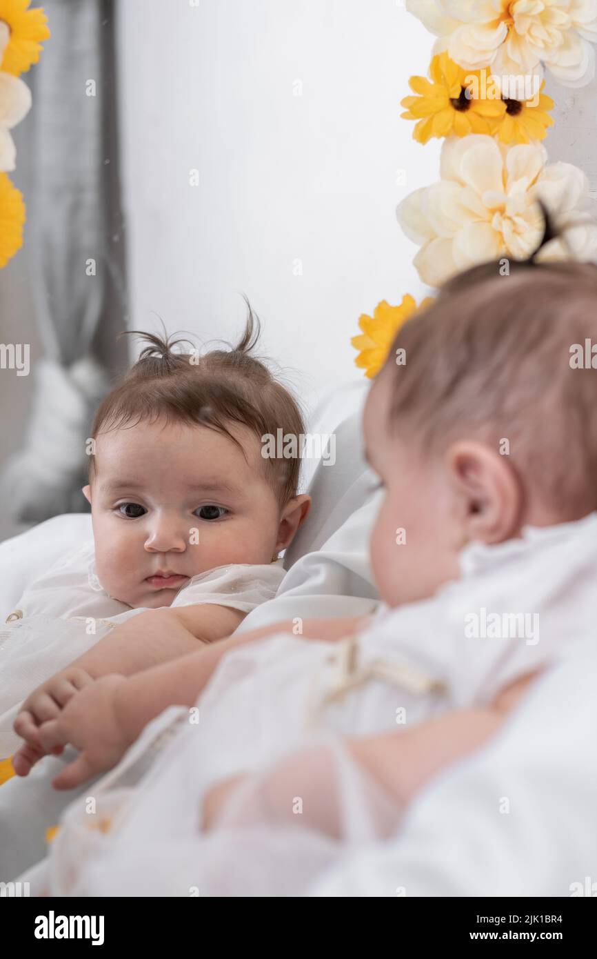 beautiful baby latina with white skin, discovering her reflection in the mirror. trying to touch her hand in the mirror while looking curiously. girl Stock Photo
