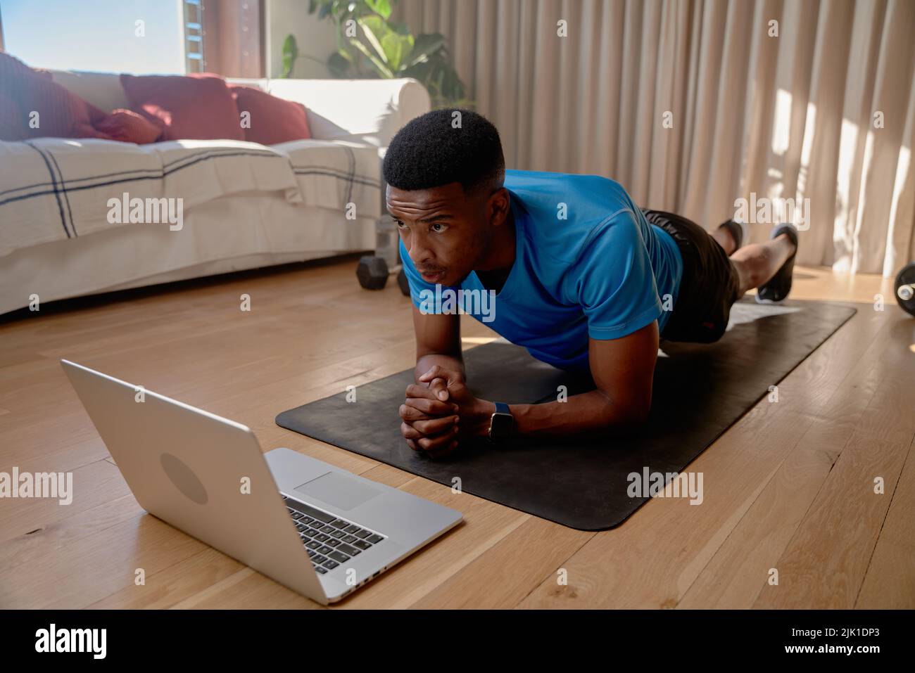 Young African American black male athlete watching workout videos on his laptop doing an online class while holding plank position. Keeping fit Stock Photo