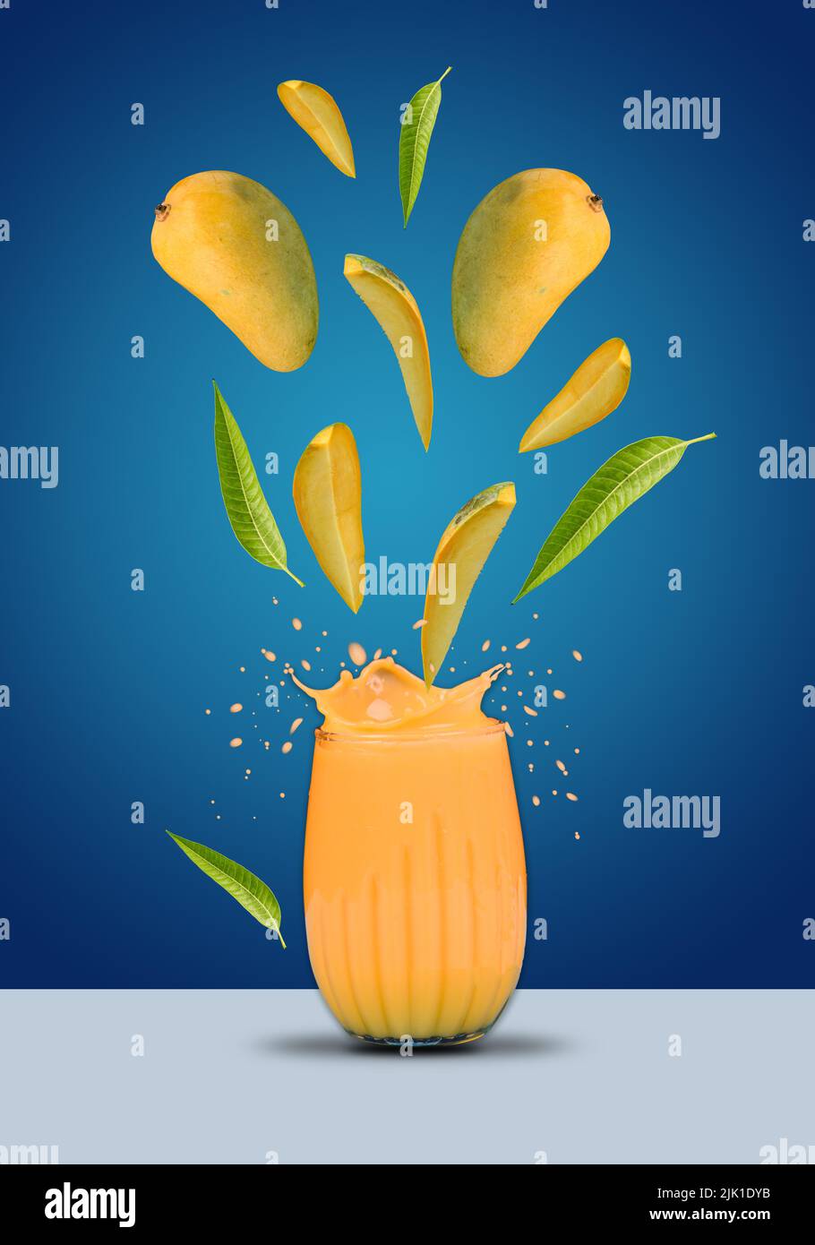 Glass of mango shake splash and hanging mangoes with leaves. Stock Photo