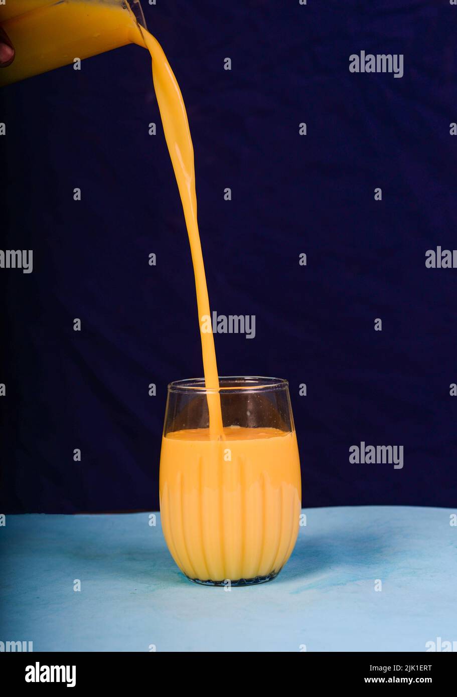 Pouring fresh milk shape of mango in isolated glass. Stock Photo