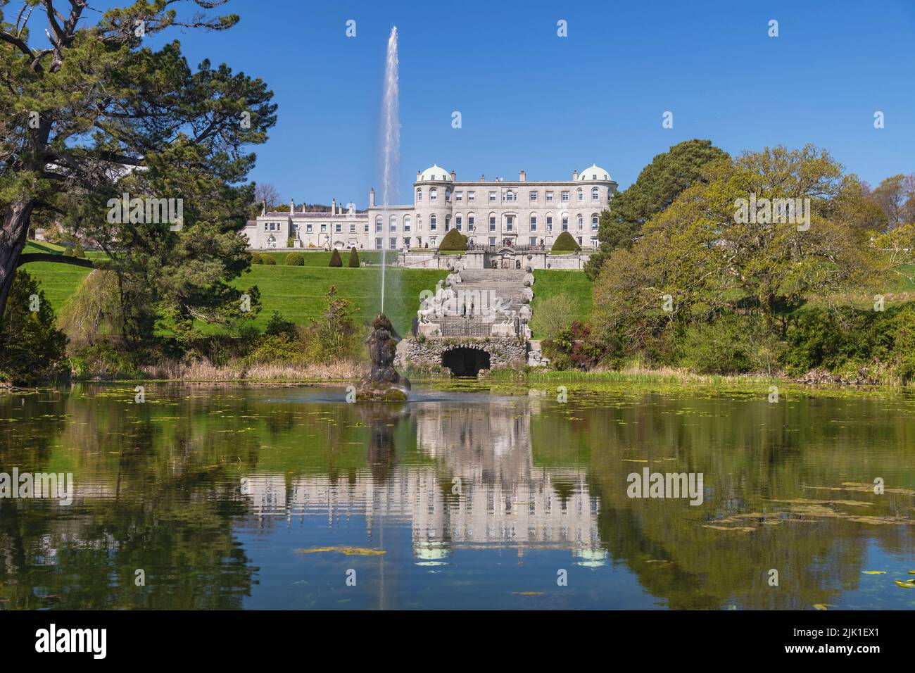 Ireland, County Wicklow, Enniskerry, Powerscourt Estate House and Gardens, Powerscourt House reflected in the Triton Lake with fountain shooting into the air. Stock Photo