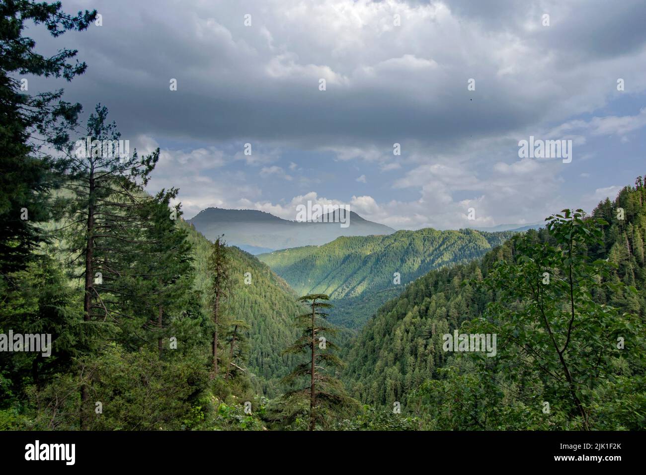 Lush green mountains valley view with dark clouds and sun rays. Stock Photo