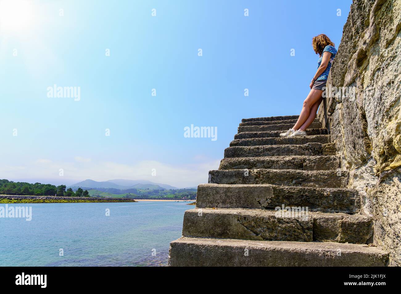 Woman at the top of some stairs looking at the beach on sunny day. Stock Photo