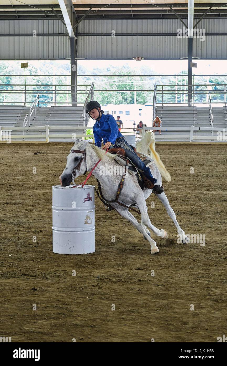 A young female equestrian on a white horse competes in a barrel racing