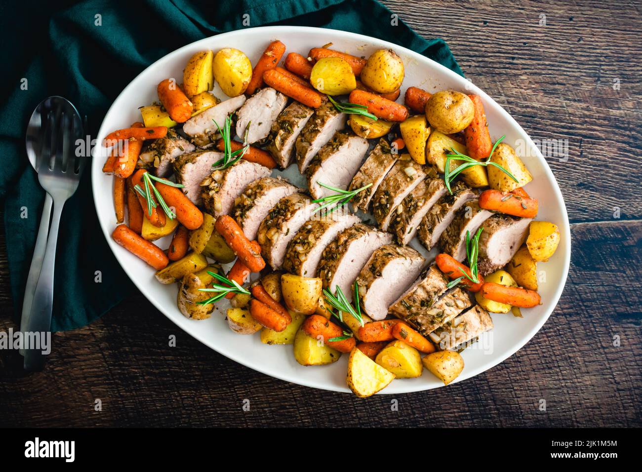 Roast Pork Tenderloin with Potatoes and Baby Carrots: Sliced pork medallions surrounded with vegetables on a platter Stock Photo