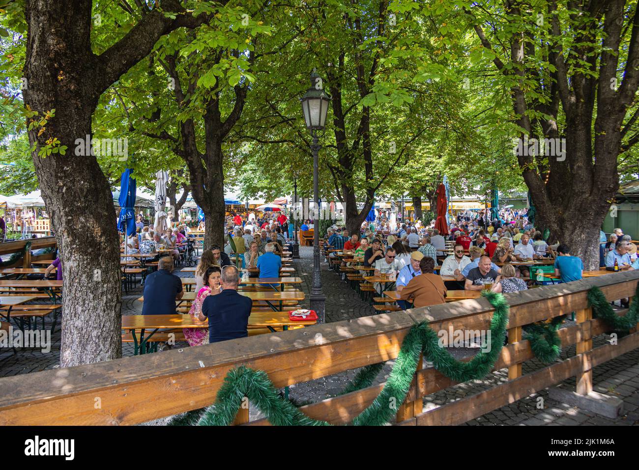 Munich, Germany - July 6, 2022: Beer garden on the viktualienmarkt at lunch time. Locals and tourist relaxing on a summer day under the shady trees an Stock Photo
