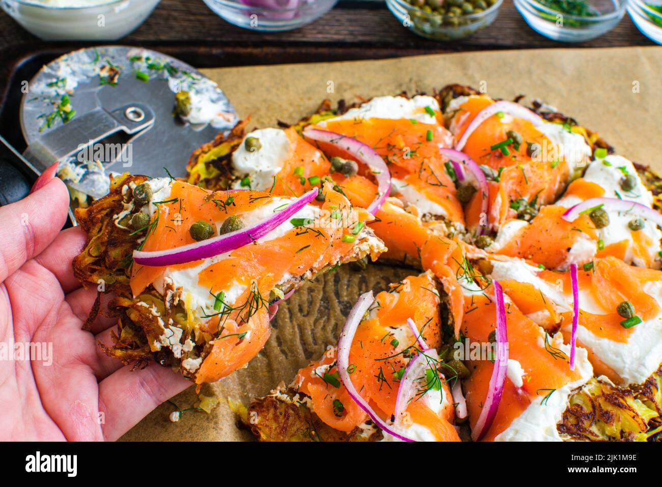 Holding a Slice of a Potato Pancake Topped with Smoked Salmon and Labneh: Latkes topped with nova, capers, red onions, and fresh herbs Stock Photo