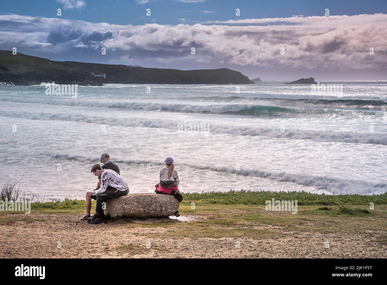 Three holidaymakers sitting on a rock overlooking Fistral Beach in Newquay in Cornwall in the UK. Stock Photo