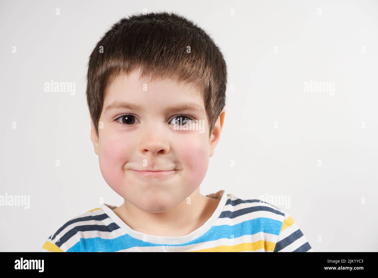 A preschool child of 4 years old with red cheeks looks into the camera, face close-up. Diathesis in children or redness of the cheeks after cold and f Stock Photo
