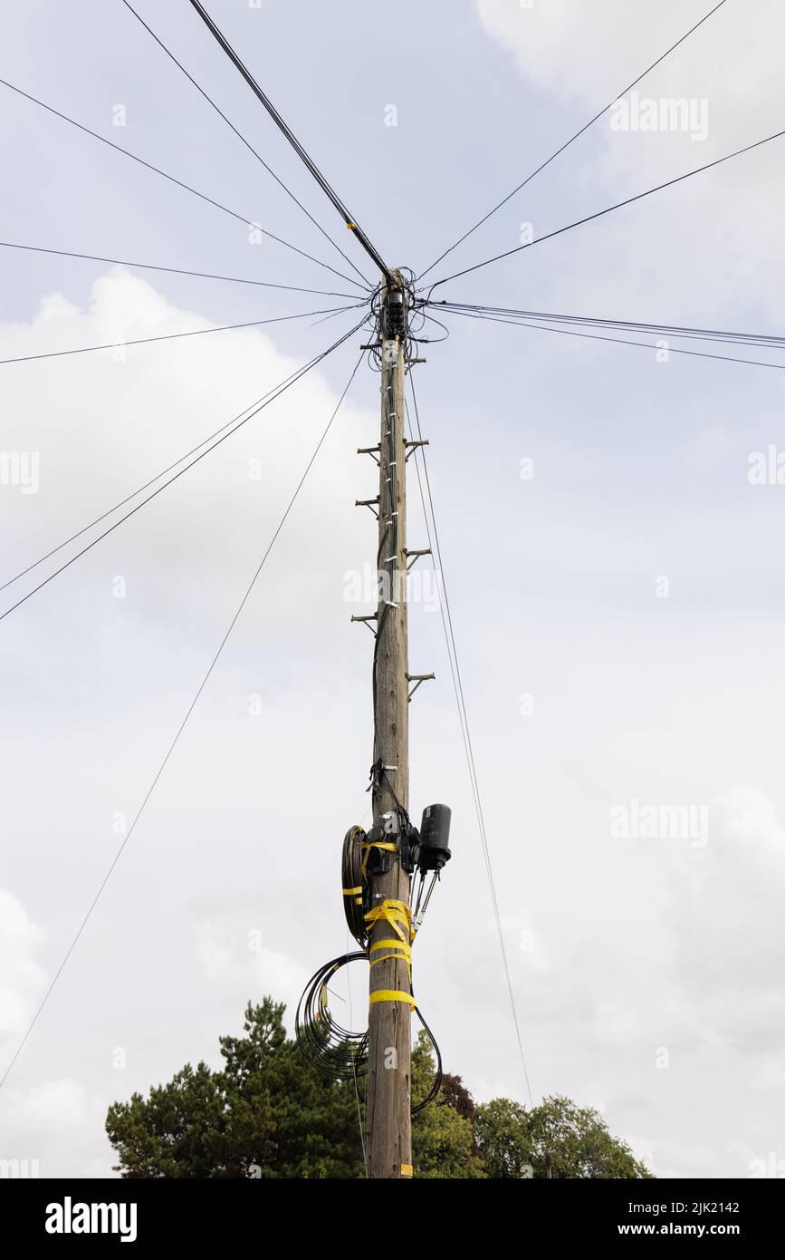 Wooden telephone pole with wires stretching out in all directions from its top. Telecomms equipment and loops of cable are attached with yellow tape. Stock Photo