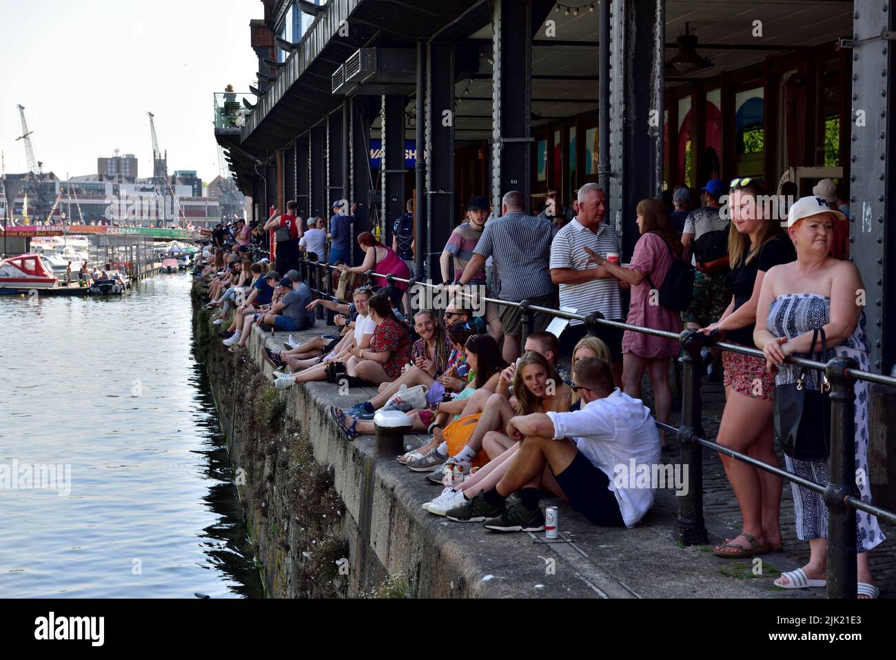 Crowd of people sitting in the shade along Bristol Harbour dock on a sunny hot day during harbour festival, UK Stock Photo