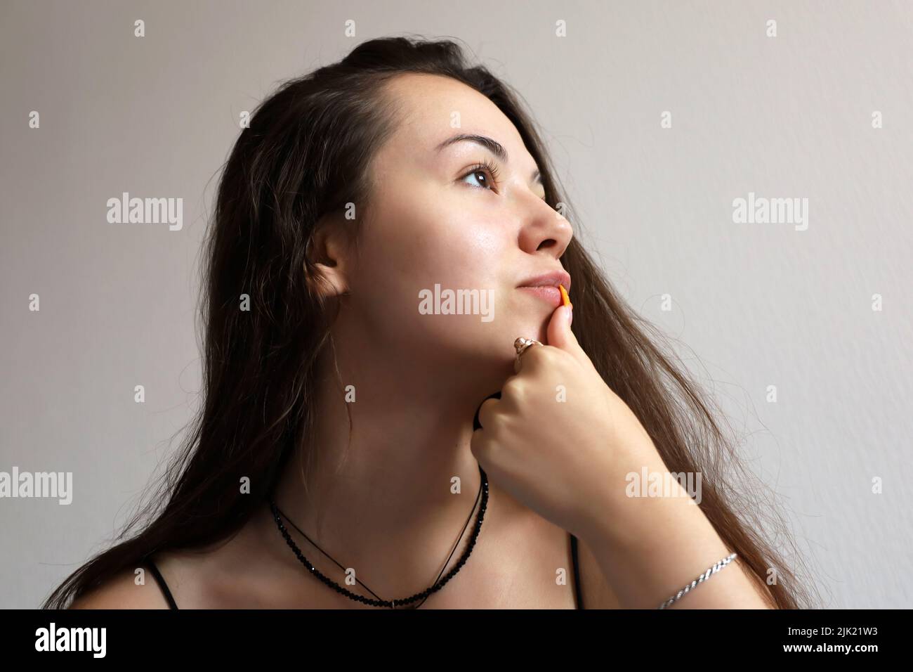Portrait of attractive young girl with long hair touching her lips with acrylic nail. Concept of female beauty, skin and hair care Stock Photo