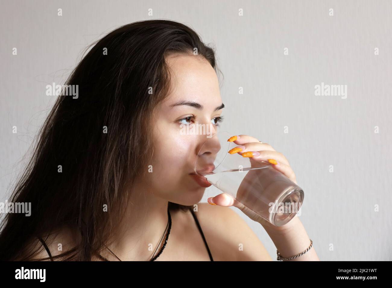 Pretty young girl with long hair drinking clean water, glass in female hands close up. Concept of thirst, diet, water purification, mineral drink Stock Photo