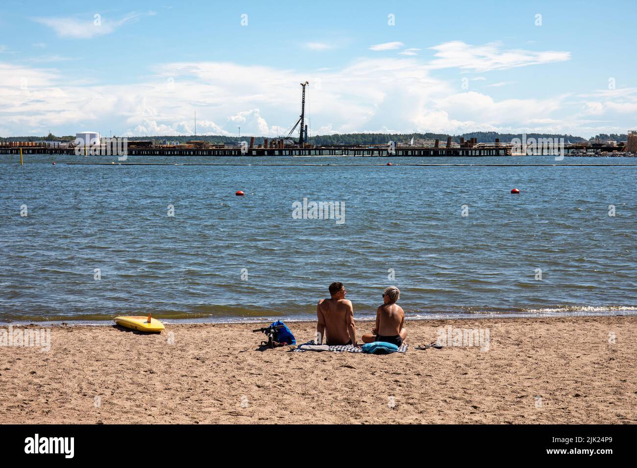 People tanning on Mustikkamaa beach while Kruununsillat bridge is under construction in the backgroung in Helsinki, Finland Stock Photo