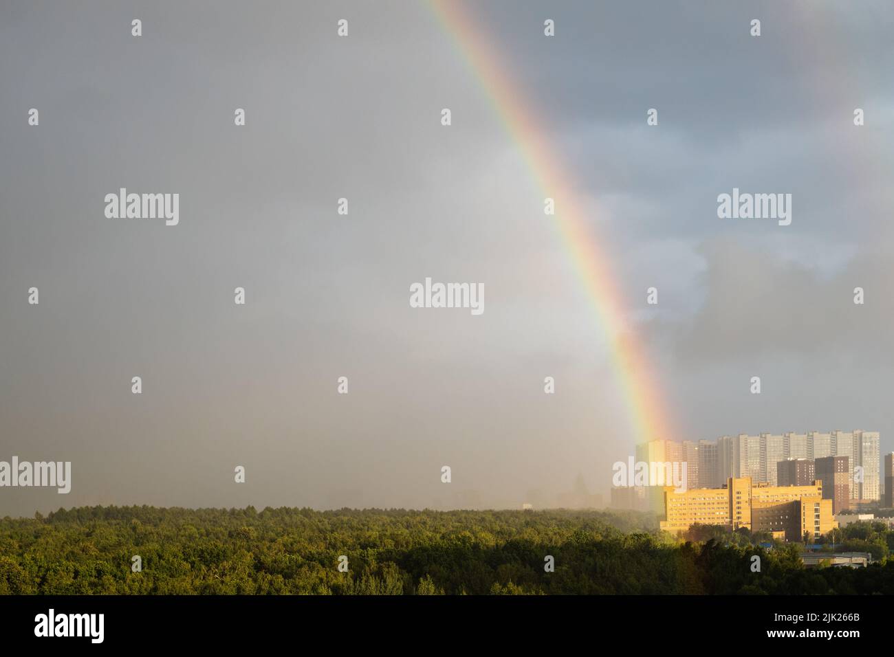 rainbow over high-rise houses and sunlit city park in rain before thunderstorm on sunny summer day Stock Photo
