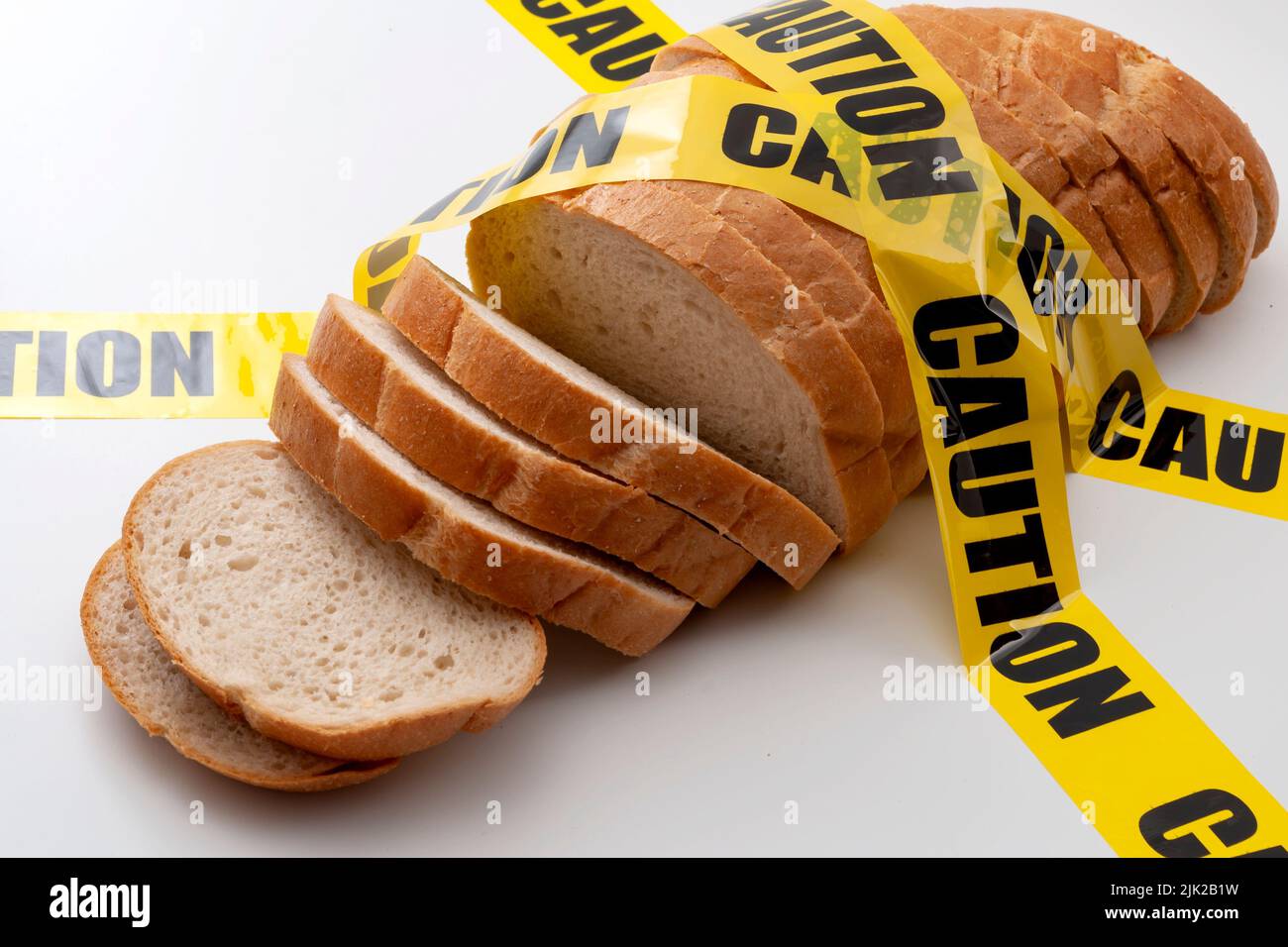 Sliced bread and yellow caution tape isolated on white background concept for food insecurity, hunger warning and hazardous processed grain Stock Photo