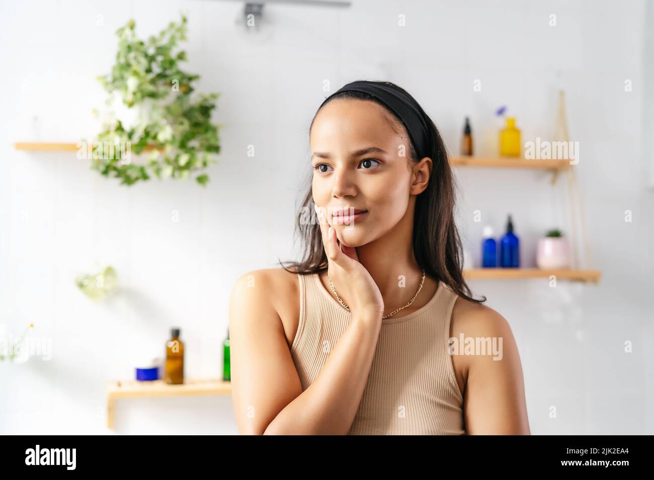 Beautiful hispanic brunette portrait against white tiled wall with cosmetics. Wellness and natural cosmetics Stock Photo