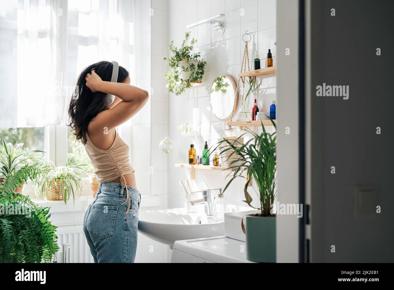 Young hispanic woman dancing with headphones in bathroom. Body positivity, confort home zone, wellness and lifestyle Stock Photo