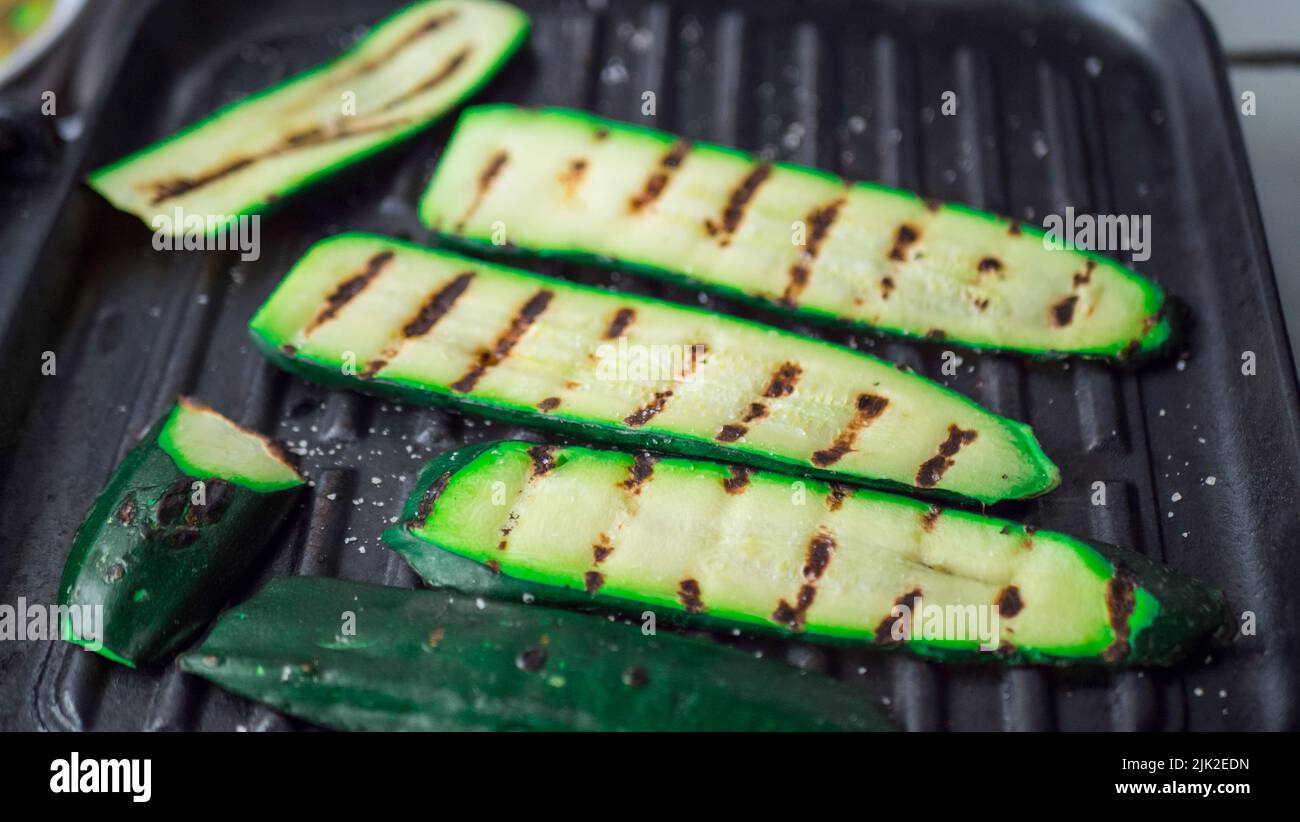 Grilled zucchini on a grill close-up. Closeup of the hands of a young woman. Selective focus Stock Photo