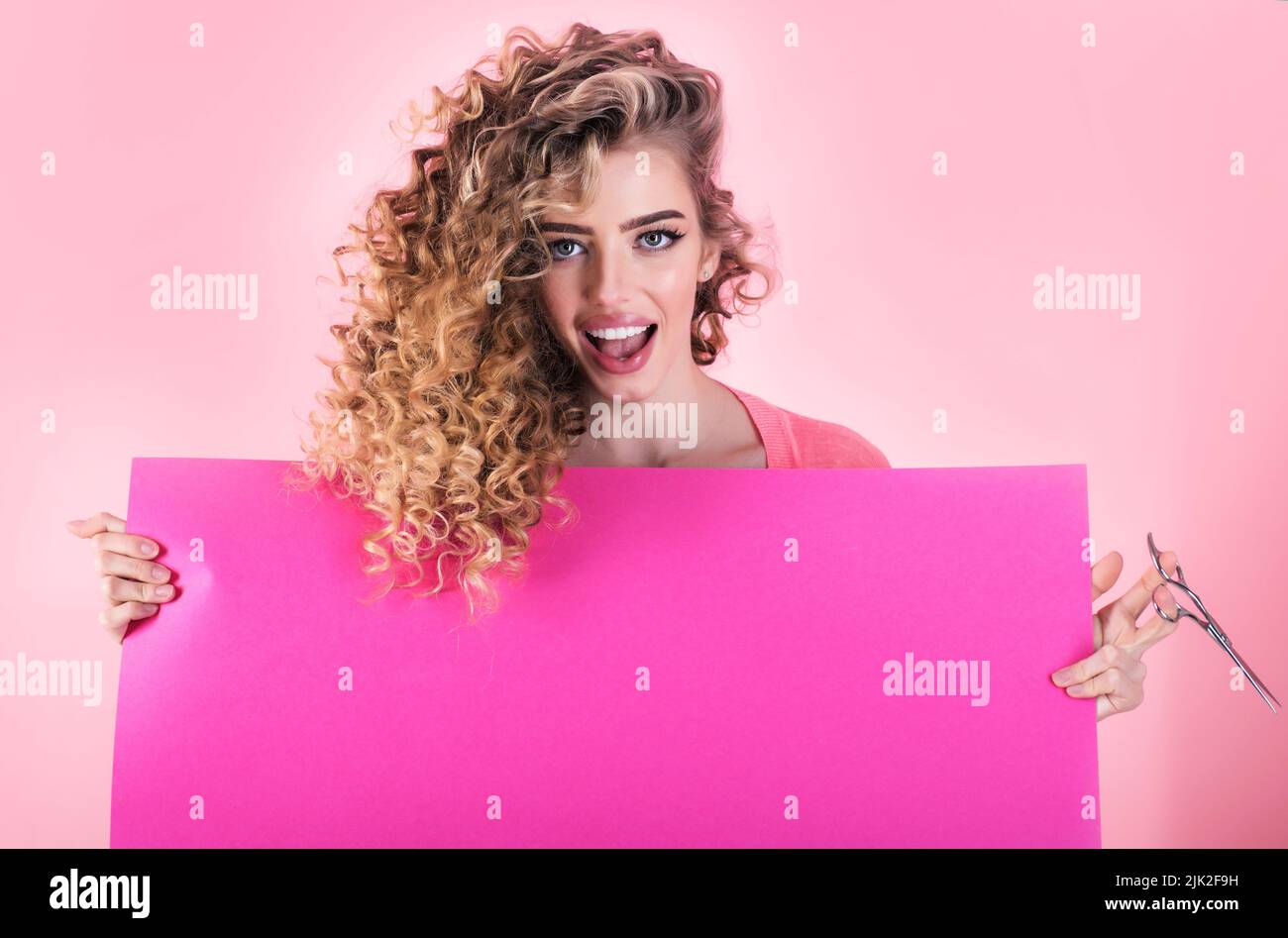 Curly hair girl with advertising board and scissors. Hairdresser. Beauty salon. Makeup and cosmetic. Stock Photo