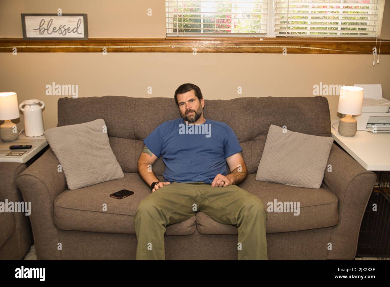 Bearded man in blue shirt relaxing on gray couch. Just chilling. Stock Photo