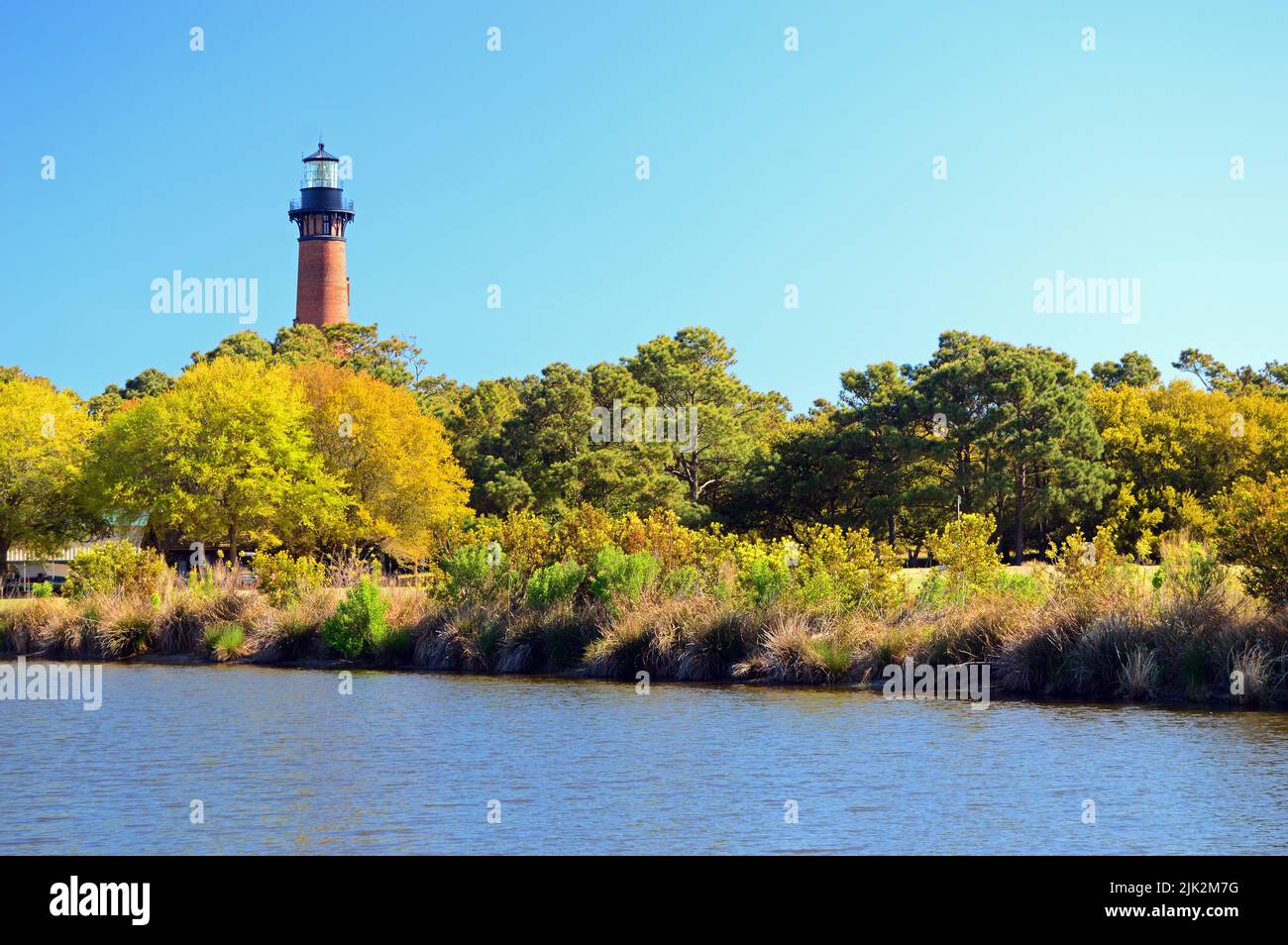 The Currituck Lighthouse peaks over the tree tops in a park on the
