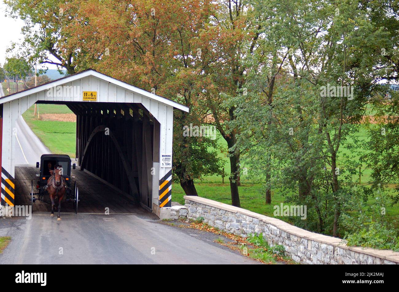 An Amish buggy rolls through a historic covered bridge in the rural areas around Lancaster County, Pennsylvania Stock Photo