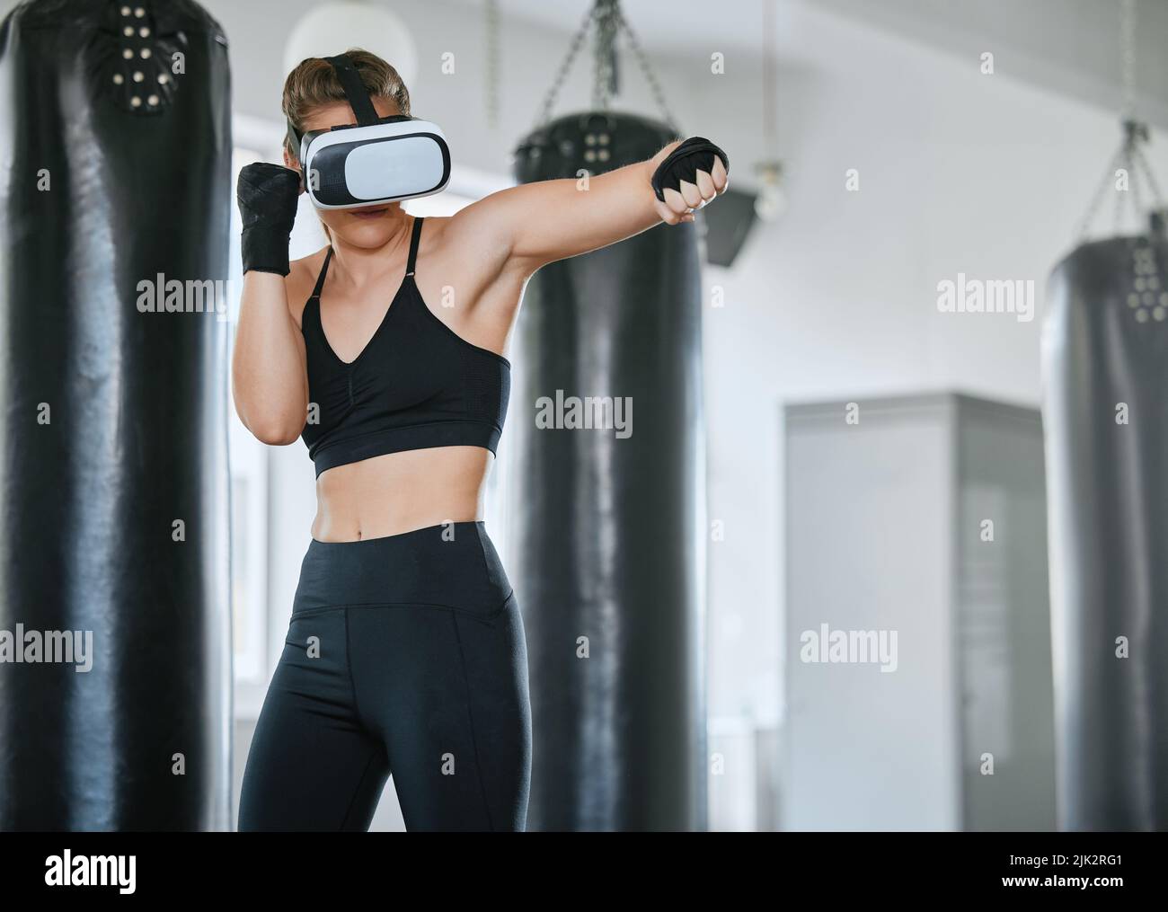 Healthy, fit and active boxing woman with a VR headset to access the metaverse while exercising, training and working out in a gym. Female boxer doing Stock Photo
