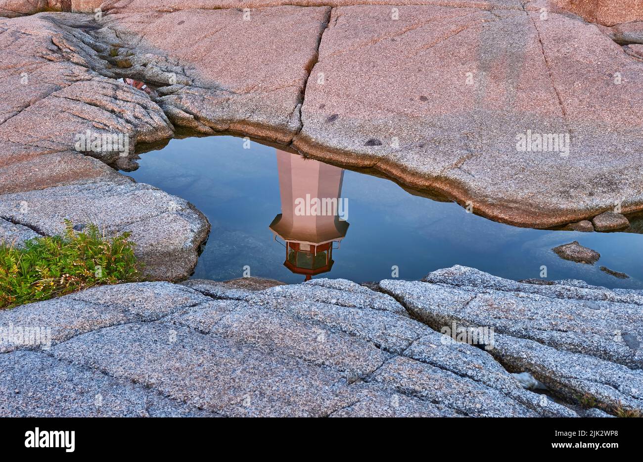 Peggys Cove Lighthouse reflected in a pool of water trapped in a depression in the rocks at sunset. Stock Photo