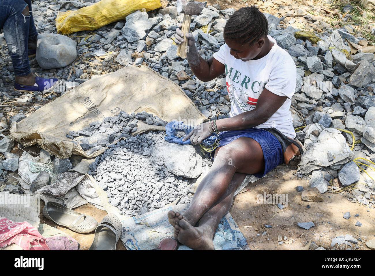 A young woman is seen seated while crushing rocks containing gold with