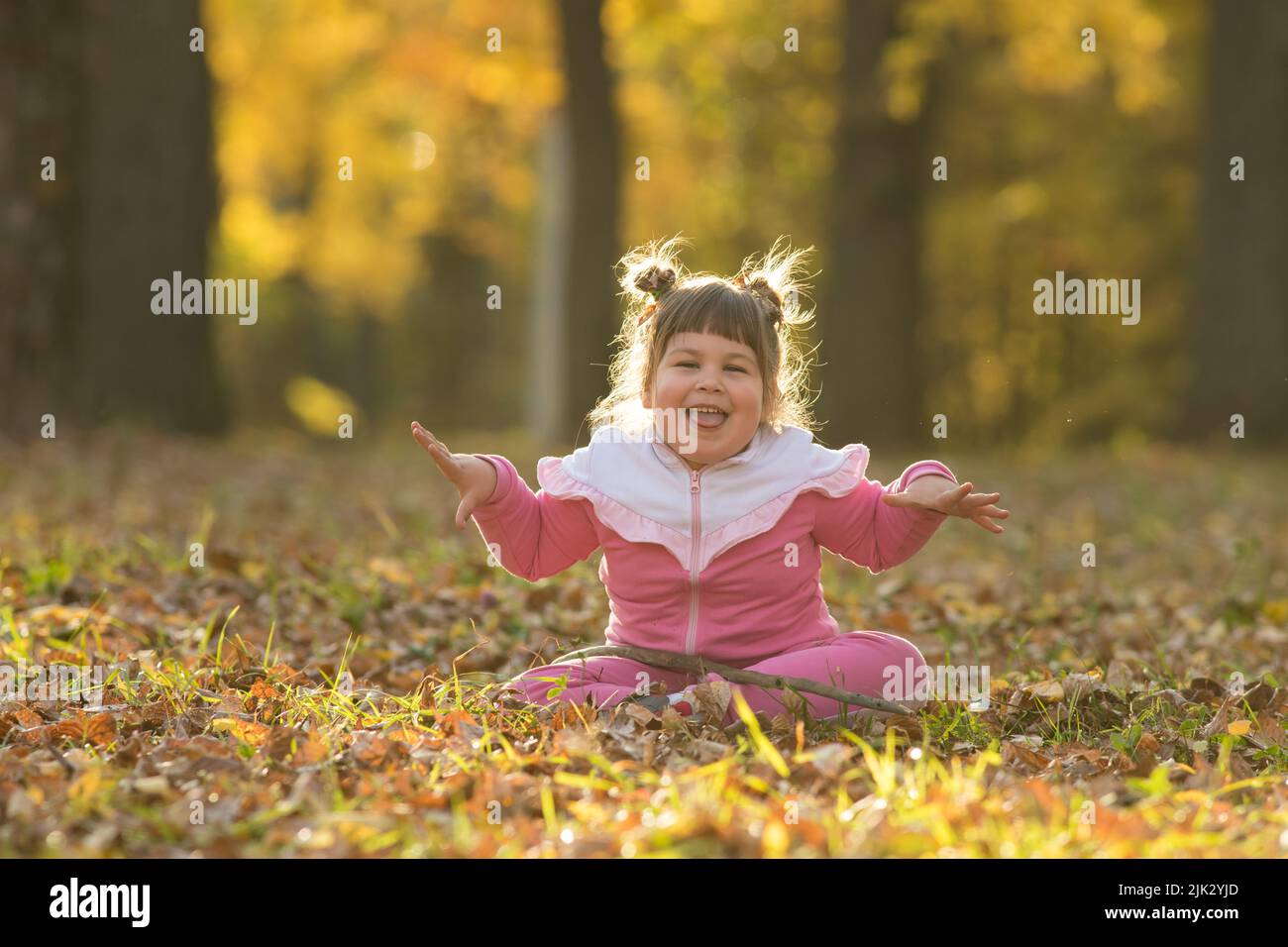 A little girl in pink costume sitting on the ground in autumn park ...