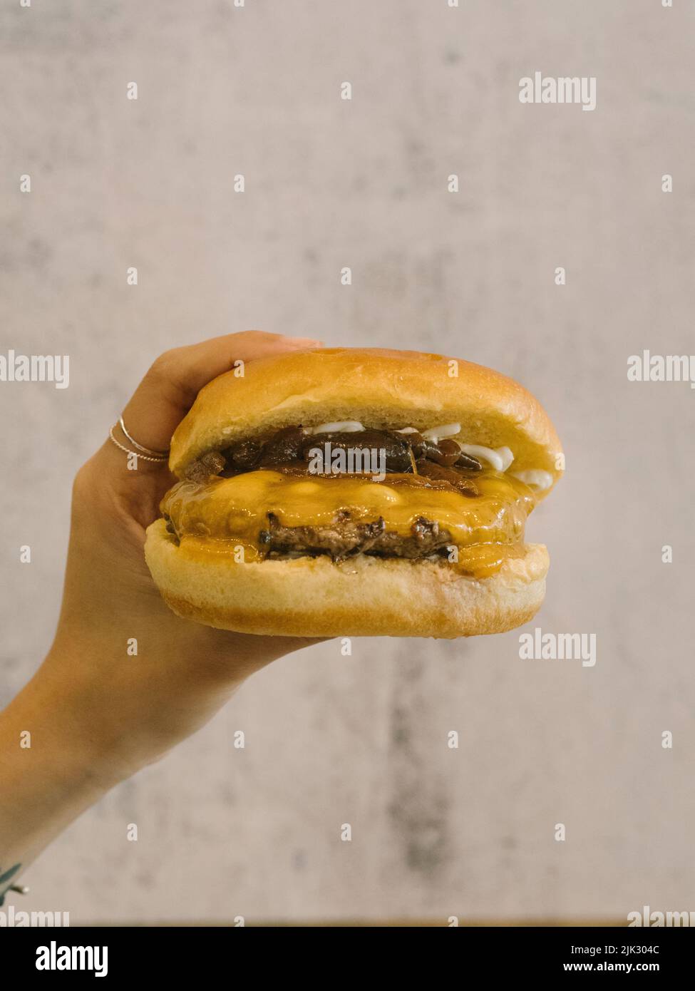 Hand holding Single cheese burger with caramalised onions Stock Photo