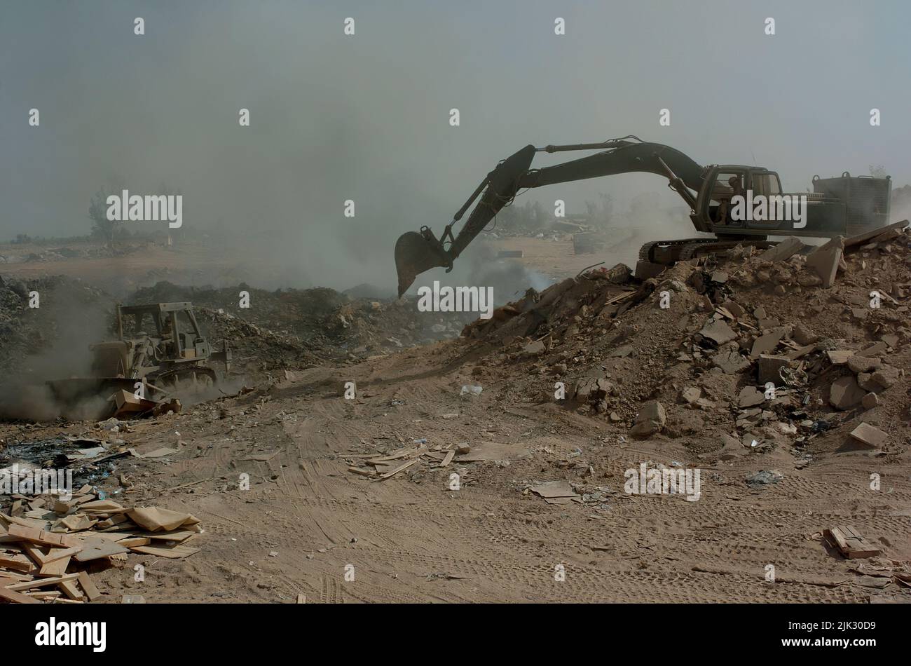 (LOGISTICS SUPPORT AREA ANACONDA, Balad, Iraq) - Soldiers from the 84th Combat Engineer Battalion use a bulldozer and excavator to maneuver trash and other burnable items around in the burn pit at the landfill here. The bulldozer is primarily used to keep refuse constantly burning, and the excavator to push dirt over chutes to make the land useable in the future. Stock Photo