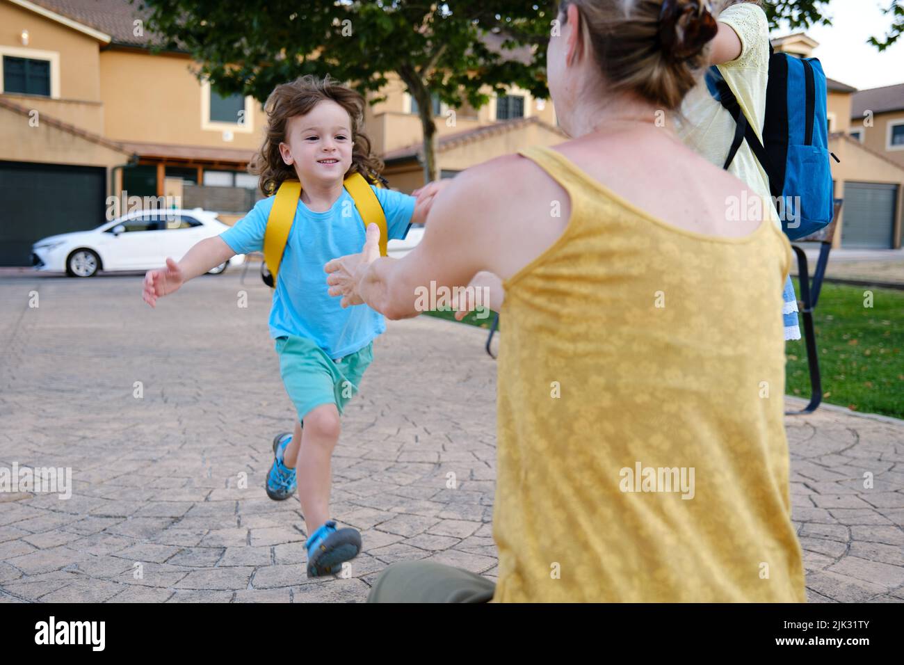 Child with backpack running to mother with open arms Stock Photo
