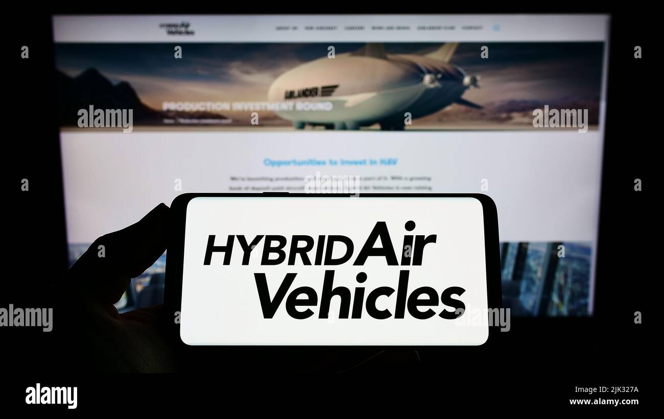 Person holding smartphone with logo of company Hybrid Air Vehicles Limited (HAV) on screen in front of website. Focus on phone display. Stock Photo