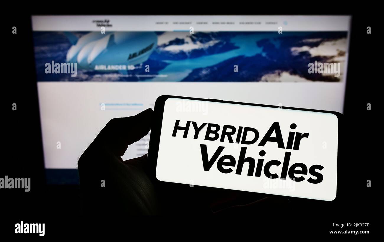 Person holding mobile phone with logo of company Hybrid Air Vehicles Limited (HAV) on screen in front of business web page. Focus on phone display. Stock Photo