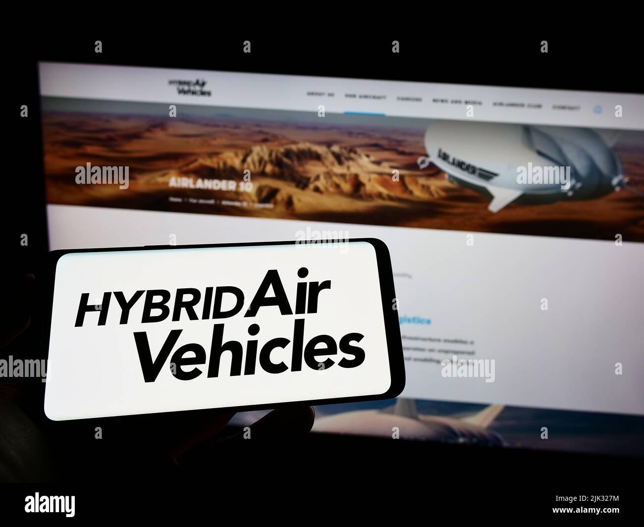 Person holding cellphone with logo of company Hybrid Air Vehicles Limited (HAV) on screen in front of business webpage. Focus on phone display. Stock Photo