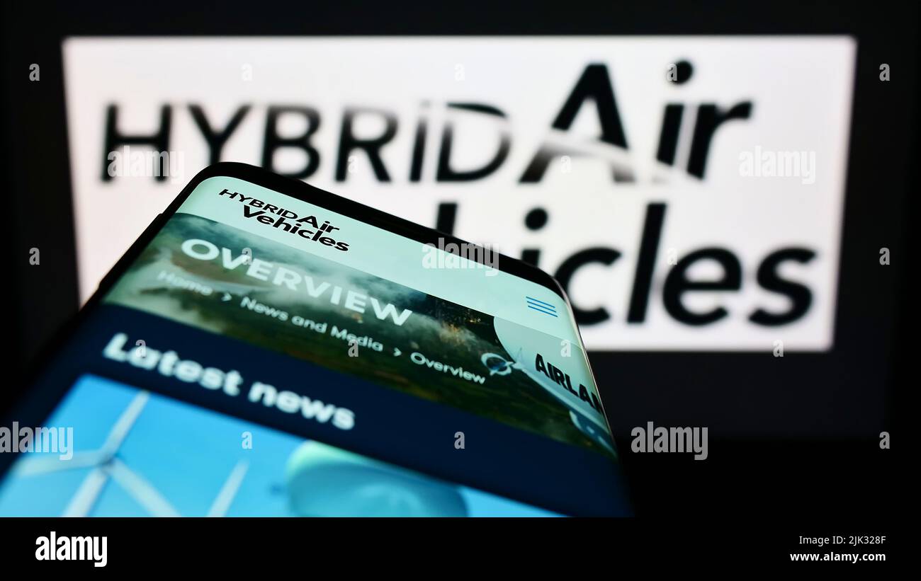 Mobile phone with webpage of company Hybrid Air Vehicles Limited (HAV) on screen in front of business logo. Focus on top-left of phone display. Stock Photo