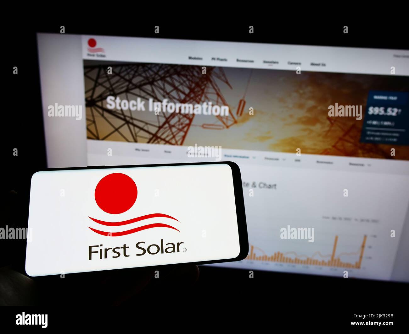 Person holding mobile phone with logo of American renewable energy company First Solar Inc. on screen in front of webpage. Focus on phone display. Stock Photo