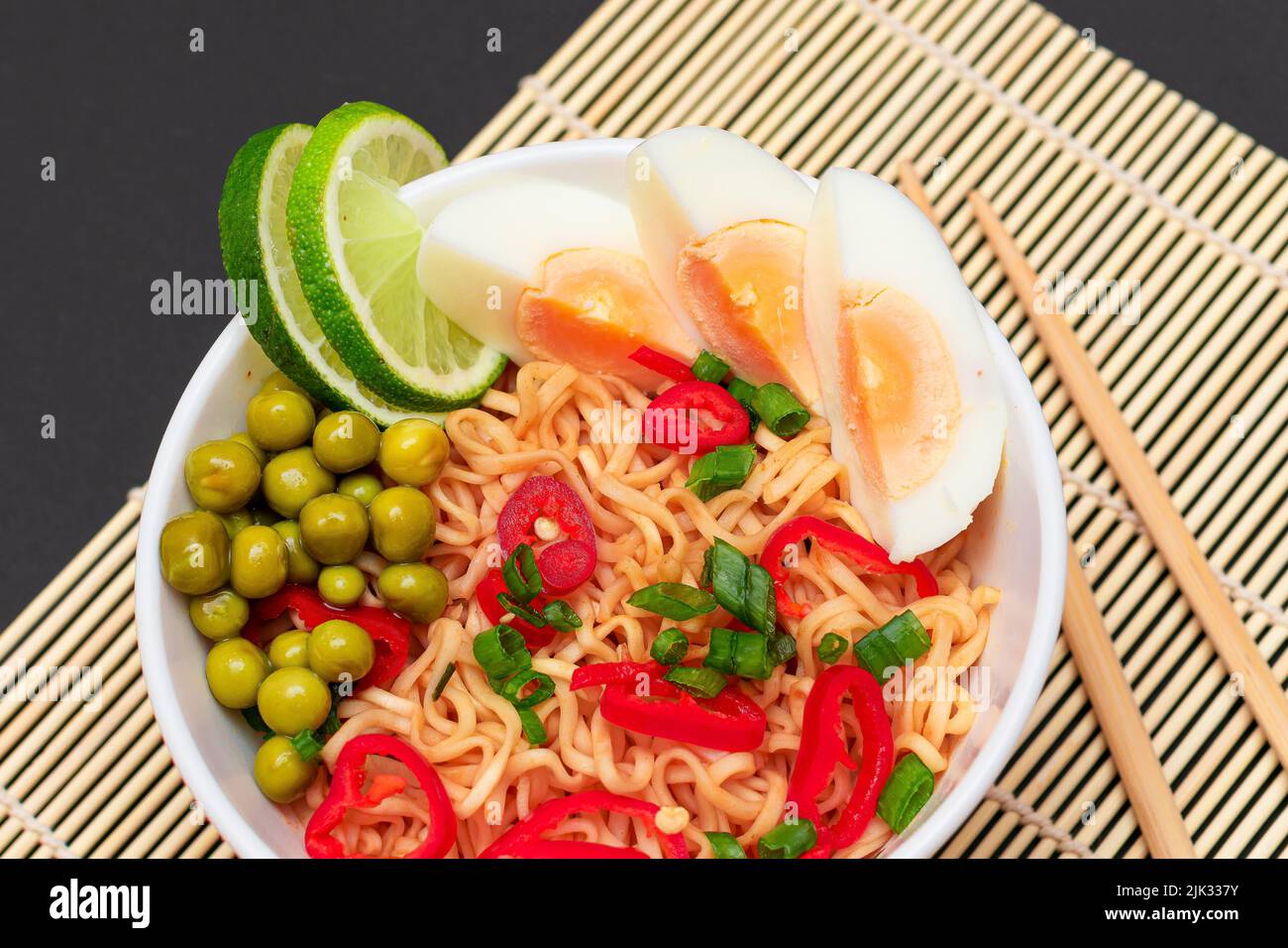 Beautiful Noodle Dish with Green Pea, Eggs, Red Hot Pepper, Greens and Lime with Chopsticks on