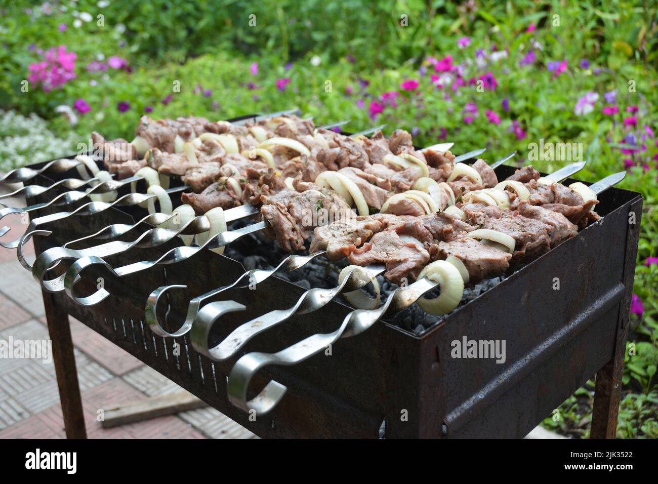 A close-up of shashlik or shish kebab, marinated chunks of meat on skewers cooked on mangal outdoors. Stock Photo