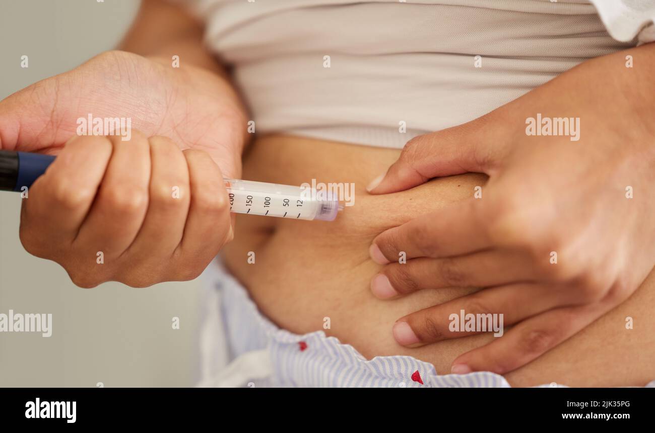 Sometimes the sugar levels are unbalanced. Closeup shot of an unrecognizable woman injecting herself in the stomach with insulin at home. Stock Photo